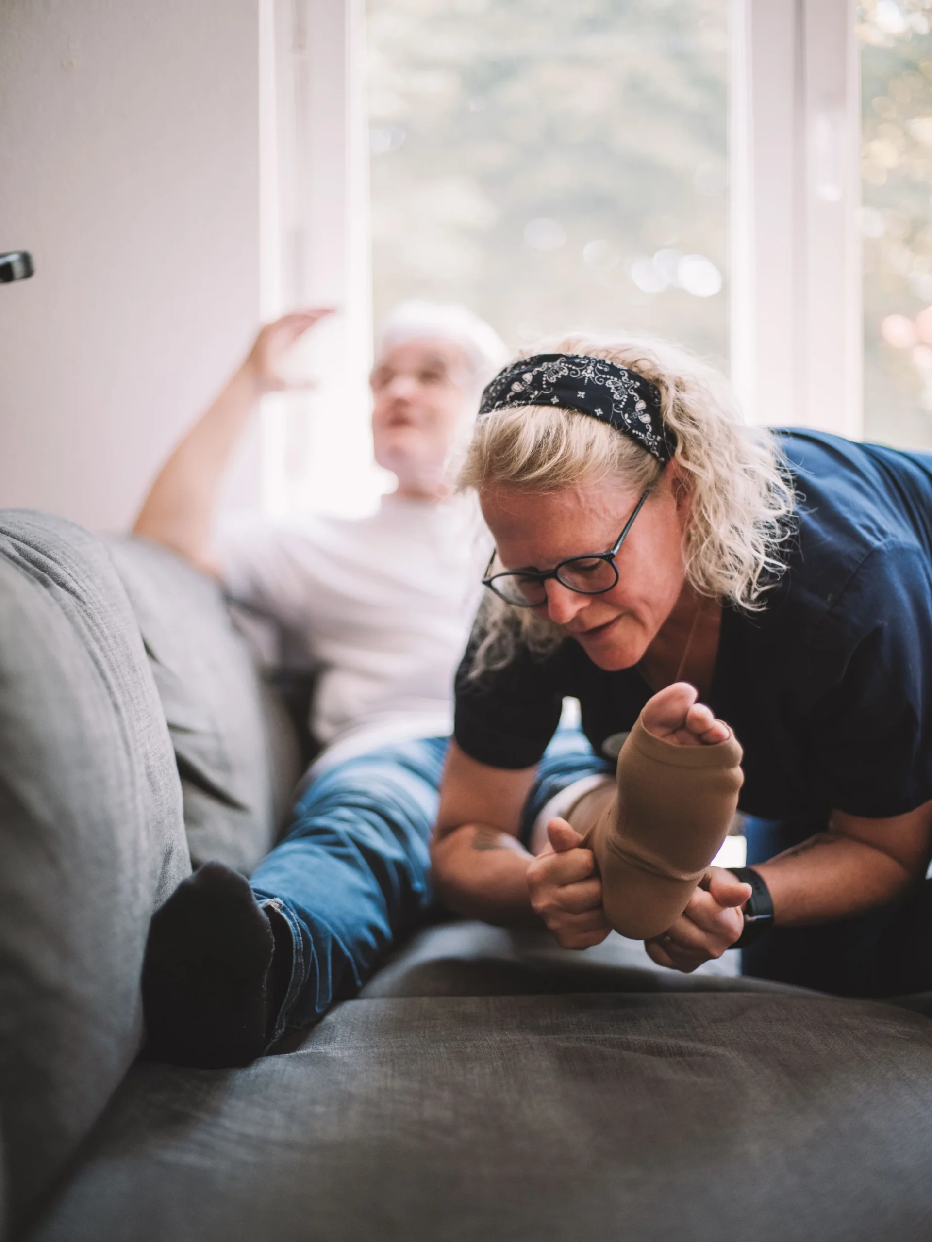 Mitarbeiter der Sozialstation hilft beim Anziehen einer Knöchelsocke